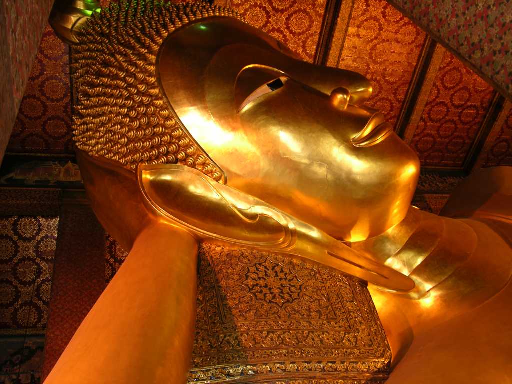 Bangkok 03 02 Wat Po Temple of the Reclining Buddha Head The Reclining Buddha represents Sakyamuni Buddha (the historical Buddha) at his death. It is said that the Buddha knew death was approaching, and asked his disciples to prepare a couch for him in a grove. He lay there, reclining on his right side, facing west, with his head supported by his hand, as he passed into nirvana. The image of the reclining Buddha is not supposed to evoke sadness, but rather encouragement that all beings have the potential to become enlightened and attain release from the sufferings which characterize the cycle of rebirth. The reclining Buddha's serene, composed, and restful demeanor (he is actually slightly smiling) is a reminder of the serenity that comes with enlightenment.